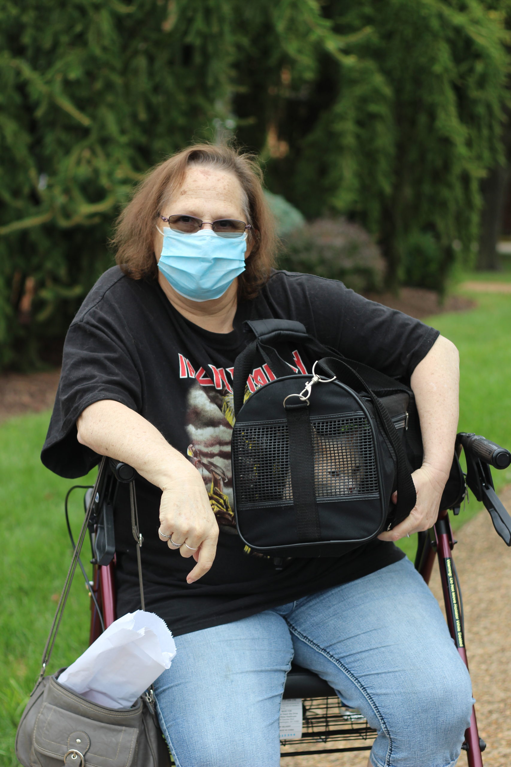 Woman in a black tshirt and blue mask holding her cat in her pet carrier